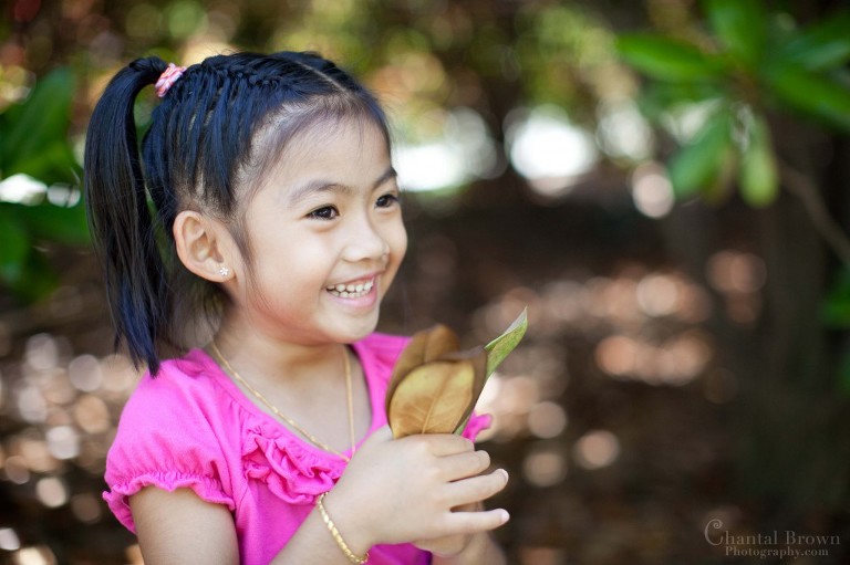 Little girl in pink shirt laughing and playing with Magnolia leaves at Dallas Arboretum garden