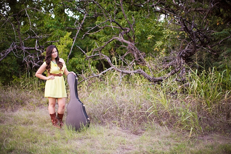 Senior portrait high school girl holding a guitar in the grass field in Wylie Texas
