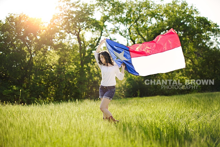 High School Senior picture of a girl holding Texas State Flag in Dallas green field at a park by Chantal Brown Photography