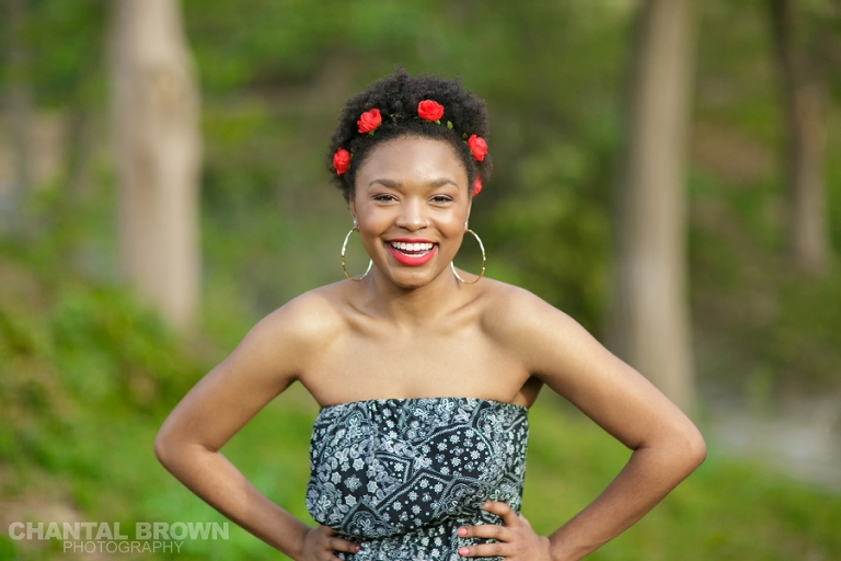 Highland Park Dallas senior portraits of a beautiful high school girl wearing a very pretty red roses head band setting on gorgeous green grass field laughing and having fun taken by Chantal Brown Photography