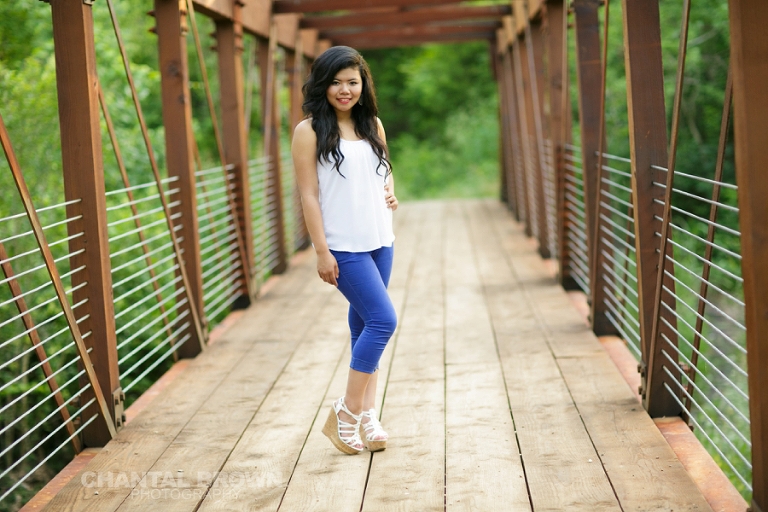 Plano senior photographer standing at a brown bridge at the park by Chantal Brown Photography.