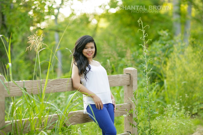 Plano senior portrait photographer a student leaning on a brown fence surrounded with gorgeous green tall grass at Richardson TX Breckinridge park by Chantal Brown Photography.