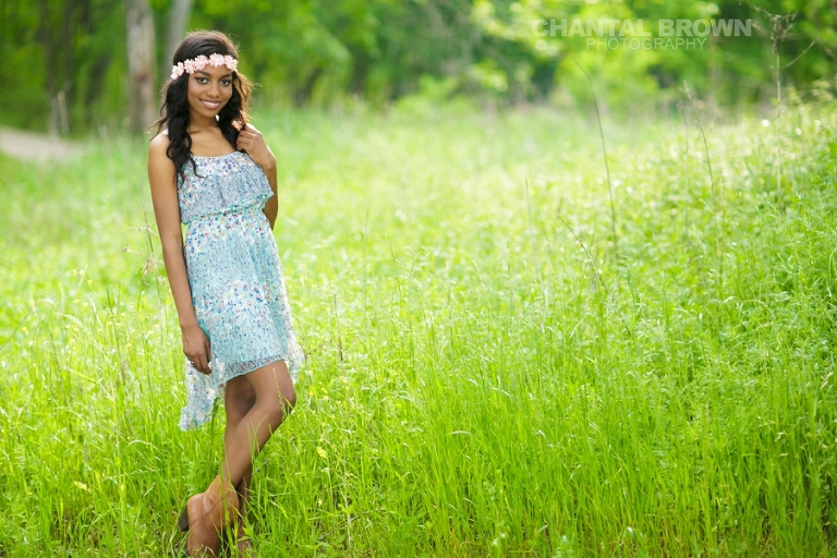 Allen senior picture of Wylie East high school senior standing in beautiful tall green grass with sun flare and wearing a pink flower head piece and baby blue dress pretending she's in Twilight movie taken by Chantal Brown Photography