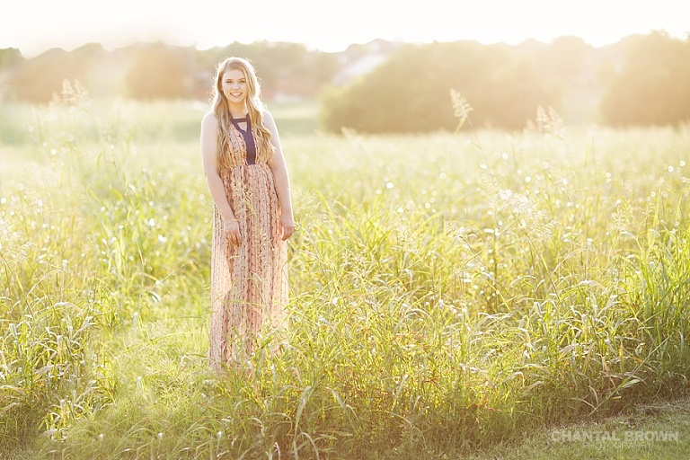 Golden sunset Dallas senior portraits with beautiful light of high school student standing in a big field taken by Dallas senior portraits photographer Chantal Brown.