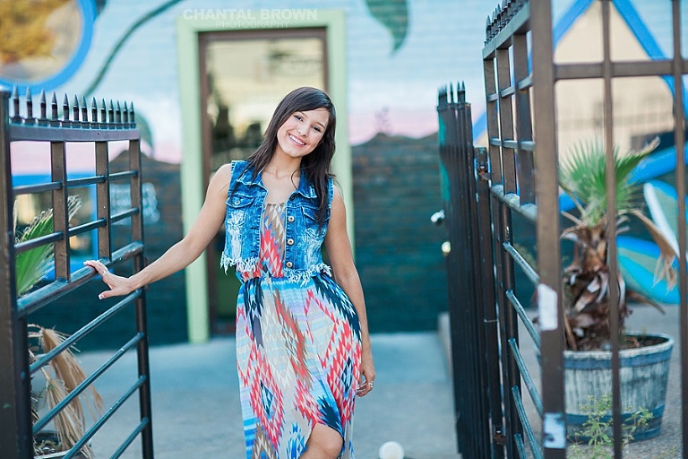 Deep Ellum senior pictures leaning on black metal fence and flower wall at Cafe Brazil in Dallas.
