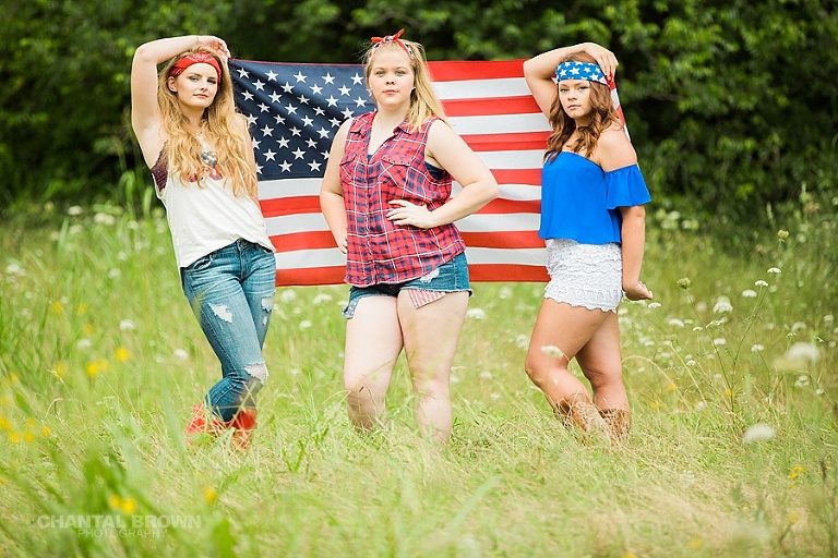 July 4th senior model group session in Dallas holding an American flag in a tall grass field taken by Chantal Brown Photography.