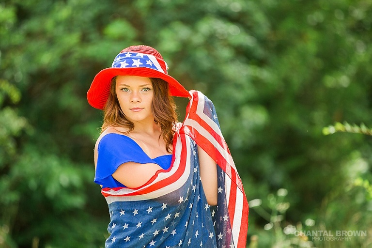 Wearing a gorgeous red, white and blue hat and wrapped around in an American flag scarf senior portraits taken outdoor in Dallas at the park with beautiful tall trees. Taken by Dallas senior portraits photographers Chantal Brown Photography.