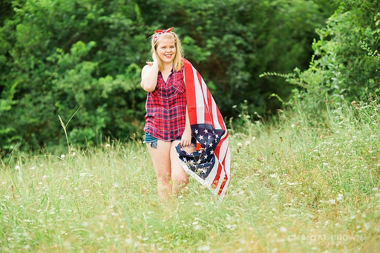Creative senior portraits photo shoot taken outdoor holding an American flag at the park with tall grass field. Taken by Dallas Chantal Brown Photography.