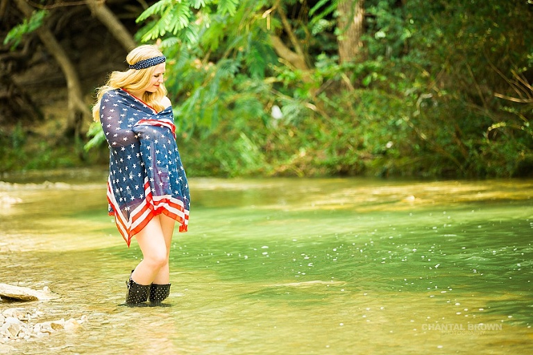 Creative senior portraits of an Allen high school senior student wrapped around American flag scarf standing in the water creek river.