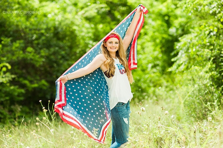 Dallas senior portraits holding an American flag scarf outdoor at a tall grass field during high noon in Dallas for a Plano East High girl. www.chantalbrownphotography.com