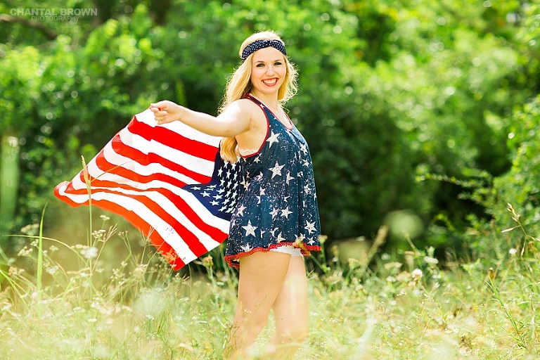 Dallas senior portraits of an Allen high school student holding and flying American flag, wearing gorgeous outfit outside a park in tall grass field. Taken by Dallas Chantal Brown Photography.