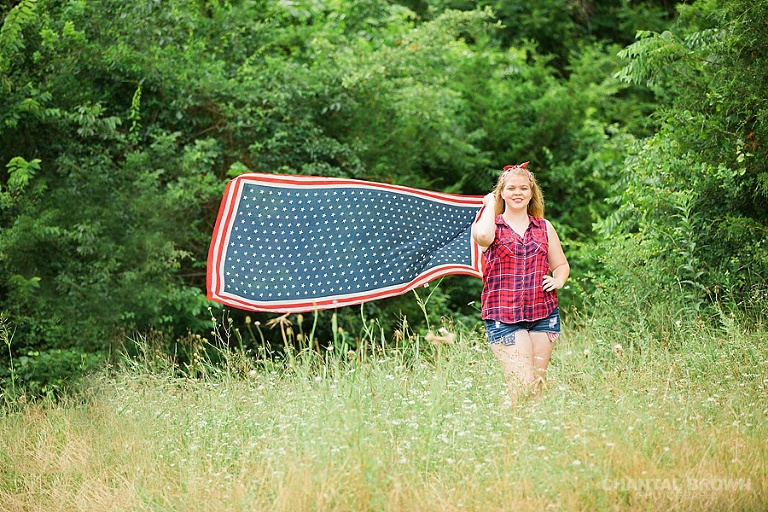 Dallas senior portraits photographers of Carrollton Hebron high school student flying an American flag scarf being very creative standing in a tall grass field in Dallas. www.chantalbrownphotography.com