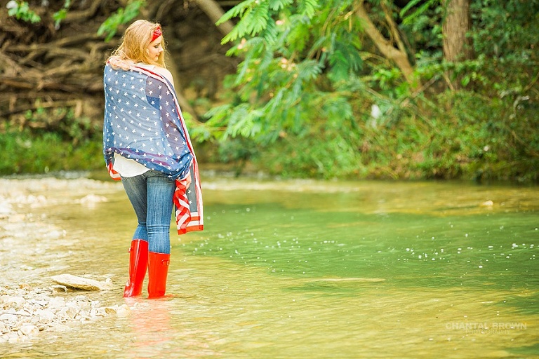 Happy 4th of July of Plano East high school student wrapped around an American flag scarf Dallas senior portraits standing in the Water River Creek. Also wearing very cute red, white and blue boots.