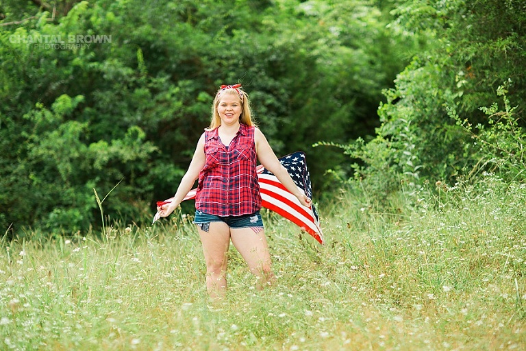Happy 4th of July holding an American flag scarf standing in the tall grass field. Taken in Dallas outdoor for Carrollton high school senior student.