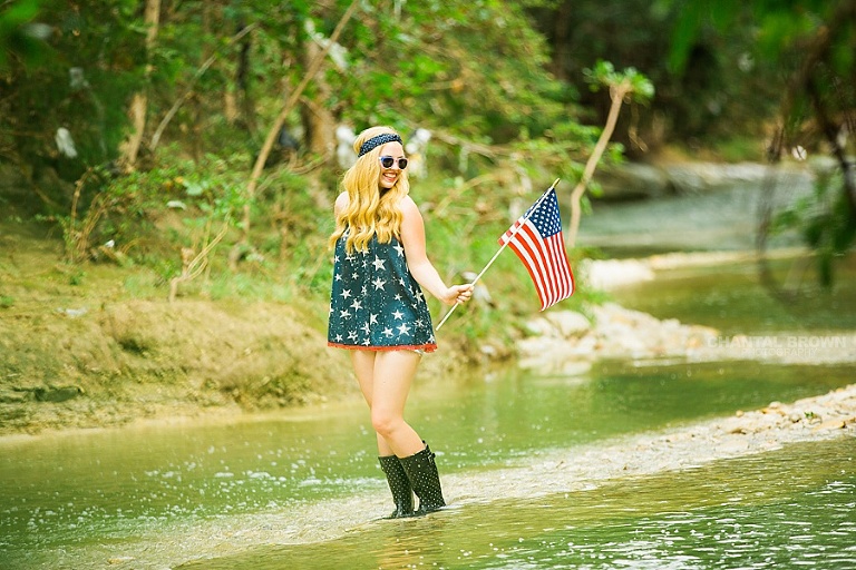 Independence Day celebration holding a small American flag senior portraits taken outdoor in Dallas in the water river creek.