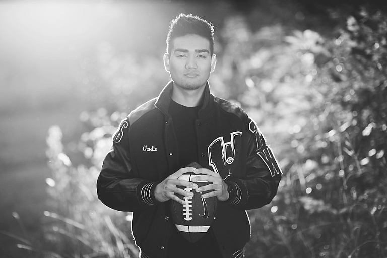 Black and white boy senior portraits holding a football during sunset.